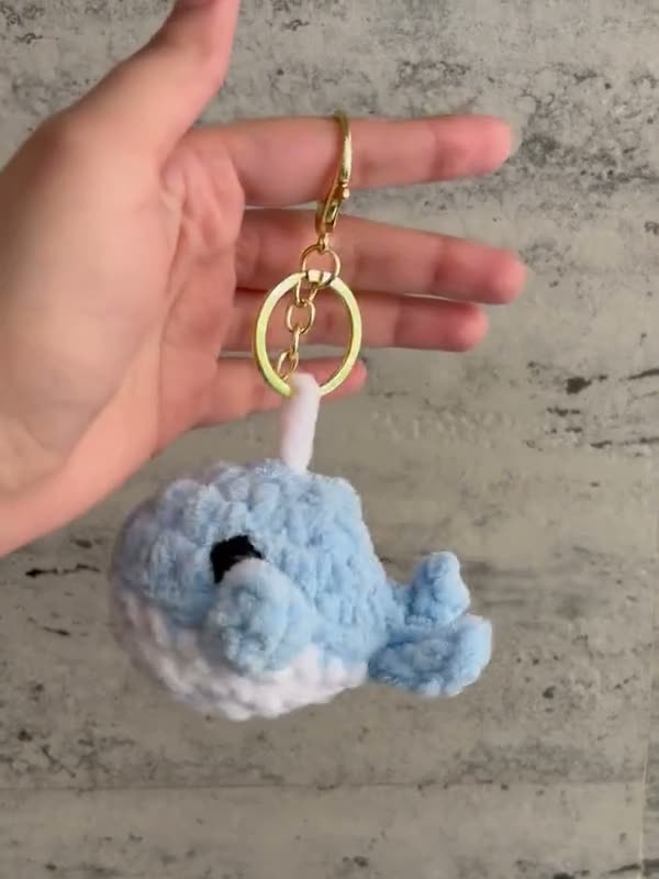 A blue crochet whale keychain with a white belly and a gold clasp