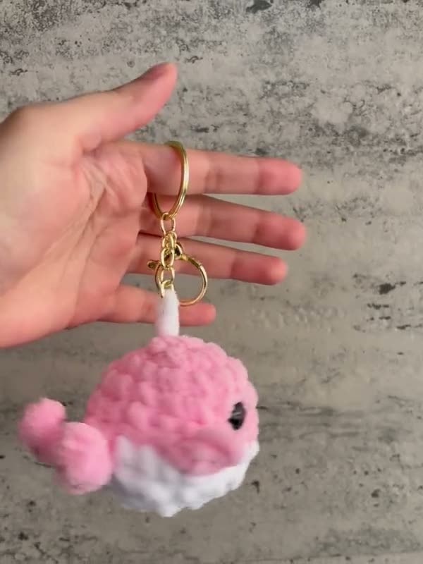 A pink crochet whale keychain with a white belly and a gold clasp