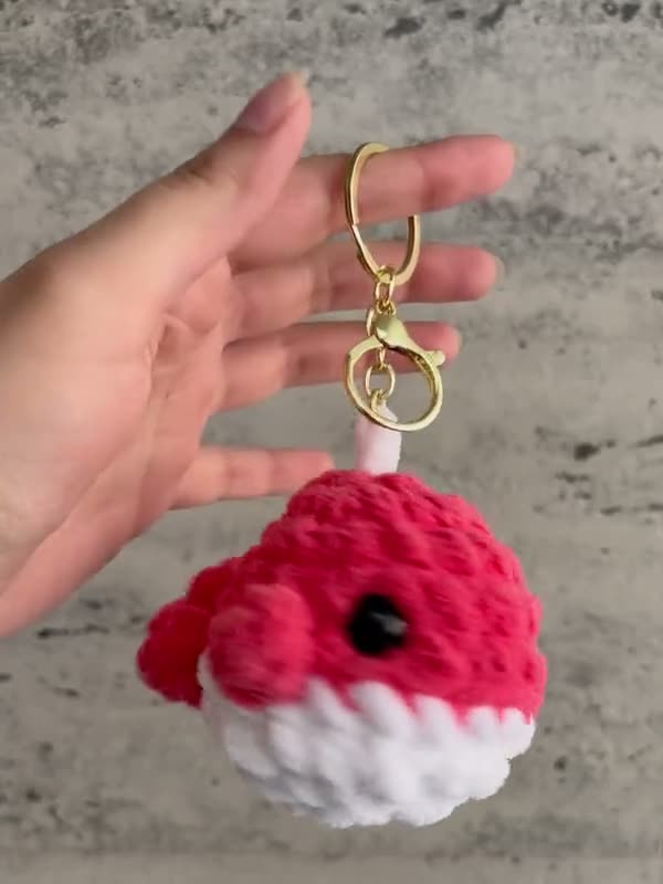 A red crochet whale keychain with a white belly and a gold clasp