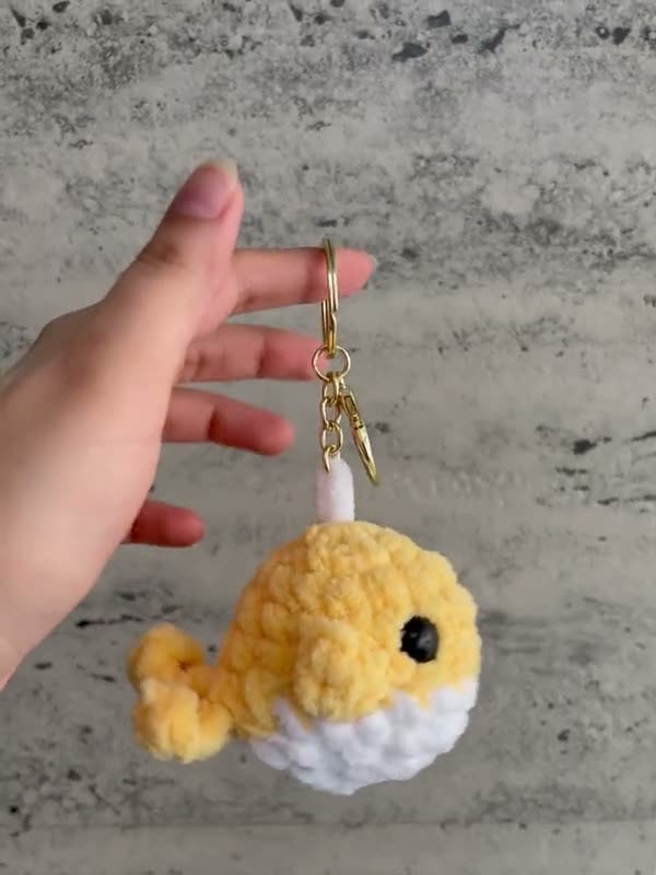 A yellow crochet whale keychain with a white belly and a gold clasp